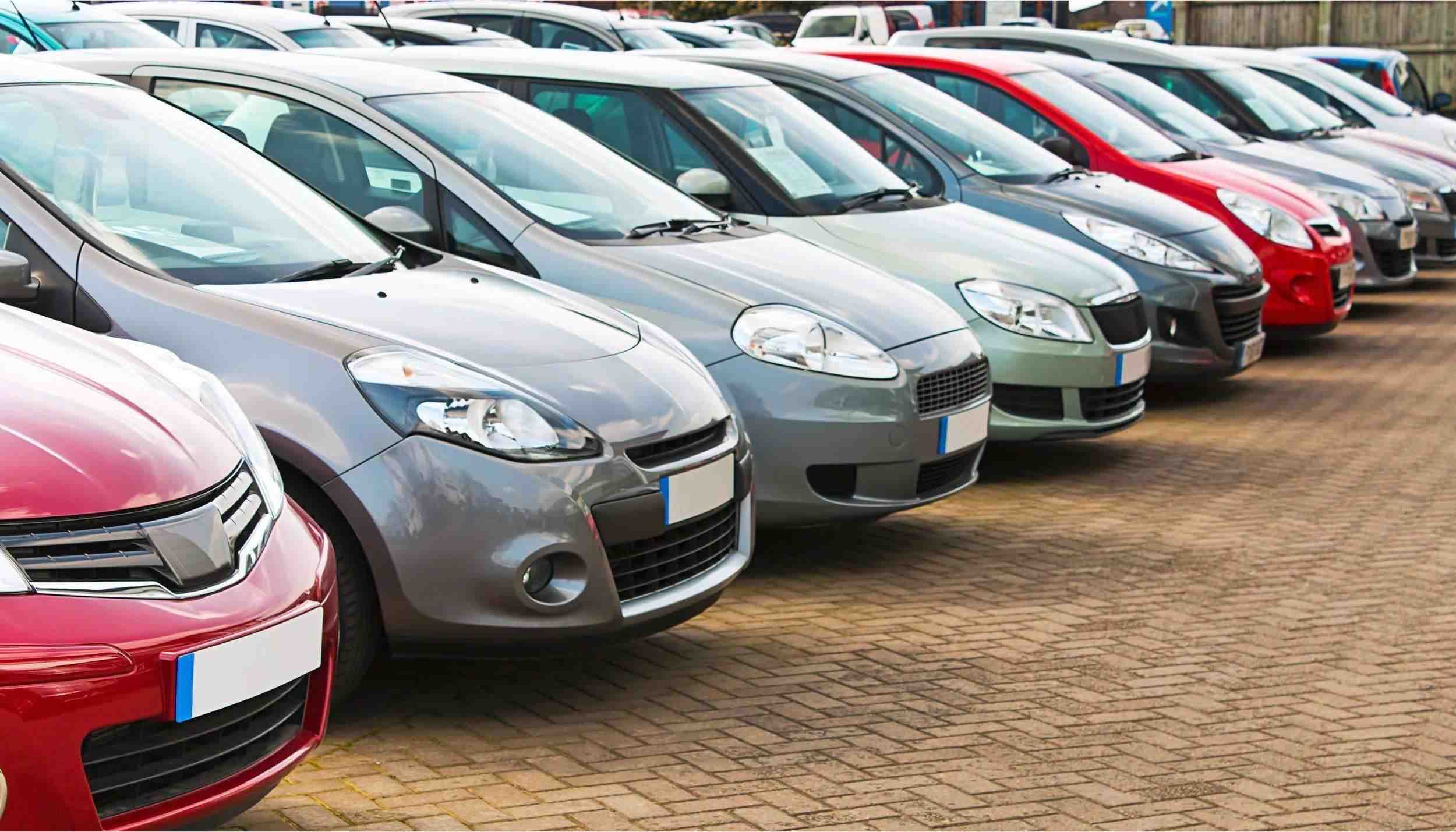 A row of parked cars neatly arranged in a spacious parking lot under clear blue skies.